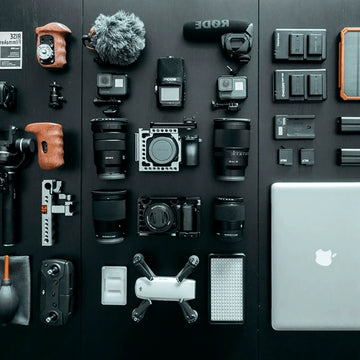 Collection of camera equipment and accessories on a black background with an Apple laptop.