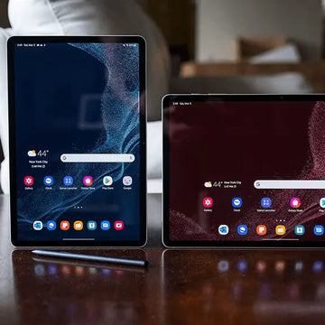 Two tablets side by side on a reflective surface with a blurred indoor background